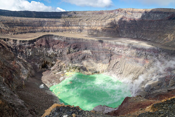Emerald green crater lake inside the active Santa Ana Volcano (Ilamatepec) in El Salvador. Layered volcanic rock lines the steep crater walls, while steam rises from the acidic lake surface. © Alira Vale