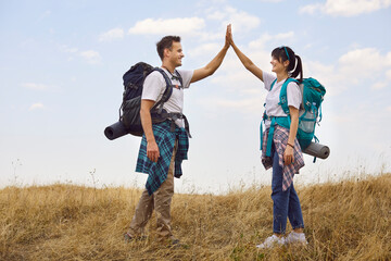 Hikers couple celebrate on forest trail in nature. Happy tourists share a high five, wearing backpack, enjoying outdoor adventure along a warm pathway. Exploration, hiking and travel concept.