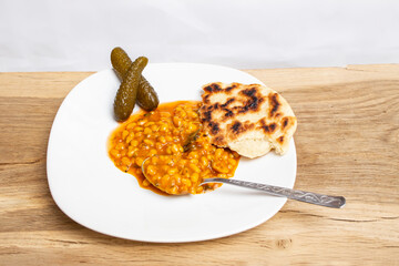 Butter beans stew with tomato sauce  , pita bread and pckled cucumbers  on wooden oak board table , side view close up