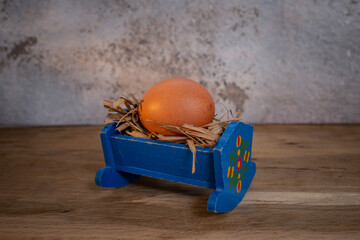 Whole egg in a baby cradle filled with hay on wooden desk, abstract pregnancy concept