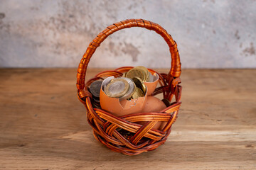 Broken egg shells filled with coins in a woven willow basket, on wooden desk, all the eggs in one basket, risky investment metaphor