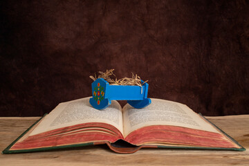 Miniature blue cradle filled with hay on a open bible book on wooden desk, christmas christian concept with vignette