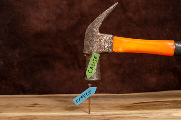 Rusty hammer and nail on wooden board, with words written on arrow sticky notes, cause and effect metaphor on brown background
