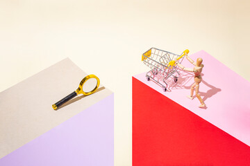 Pop art style photography of a wooden mannequin pushing a shopping cart and a magnifying glass on pink , red and beige paper background arranged as a geometric podium, abstract consumerism metaphor