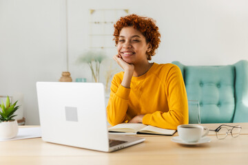 Smiling African American girl using laptop at home office typing chatting reading writing email. Young woman having virtual meeting online chat video call conference. Work learning from home