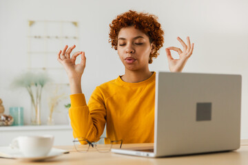 No stress keep calm. Mindful African businesswoman practices breathing exercises at home office. Peaceful young woman at workplace enjoy yoga eyes closed hands in chin mudra gesture. Office meditation