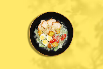 Classic Caesar salad with grilled chicken, quail eggs and parmesan on yellow background