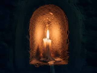 Glowing candle in rustic niche with dripping wax and shadow