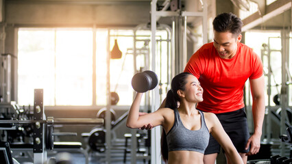 A male trainer is demonstrating the method and steps for a dumbbell exercise to a woman in the gym, Exercise concept, health maintenance, Horizontal image, vertical image.