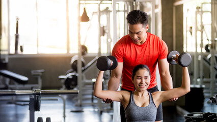 A male trainer is demonstrating the method and steps for a dumbbell exercise to a woman in the gym, Exercise concept, health maintenance, Horizontal image, vertical image.