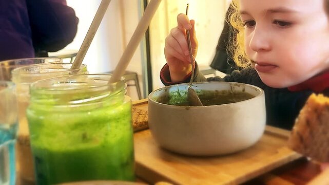 Child eating green vegetable soup in a cafe