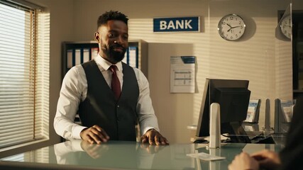 Bank teller helps customer at service counter. Smiling teller assists client with banking transaction. Professional banker serves customer at bank desk. Teller provides financial service at counter.