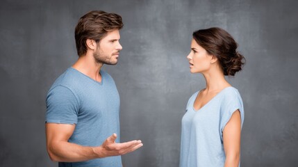 Young couple in casual attire engaged in a heated argument, showcasing emotional conflict and tension, with a neutral gray background enhancing the dramatic atmosphere