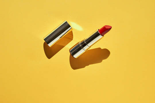 Red lipstick on bright yellow background with silver cap highlighting bold color and elegant design.