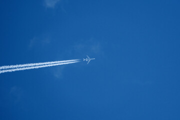 Passenger plane in flight against blue sky and clouds. Commercial airplane flying in the clear blue sky with white clouds and vapor trail.