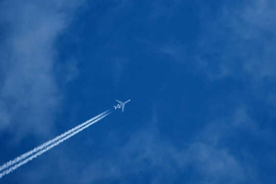 Passenger plane in flight against blue sky and clouds. Commercial airplane flying in the clear blue sky with white clouds and vapor trail.