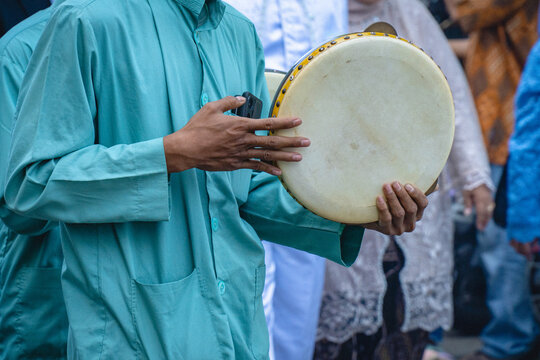 A man playing traditional frame drum during a cultural or religious gathering, capturing musical performance, rhythm, and community celebration in Indonesian tradition.
