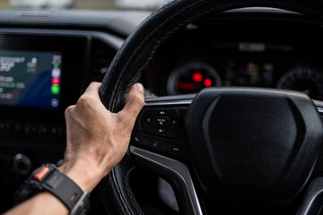 Close-up of Driver's Hand on Steering Wheel of a Modern Car,A close-up shot of a male driver's hand holding a leather steering wheel while driving a modern vehicle. 