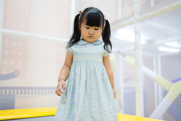 Cute little Asian girl in floral dress playing on indoor trampoline,A portrait of a charming young...