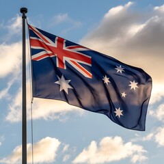 The Australian flag waving in the wind against a blue sky with clouds