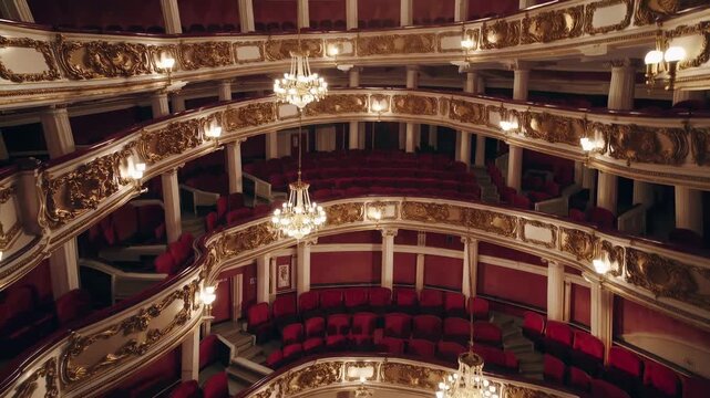 The ornate theater features multiple balconies, showcasing elegant architecture and red seating. The chandeliers illuminate the grand setting, enhancing the theater's rich design.