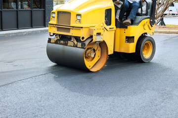 Yellow steamroller machine is flattening fresh asphalt at construction site © ungvar