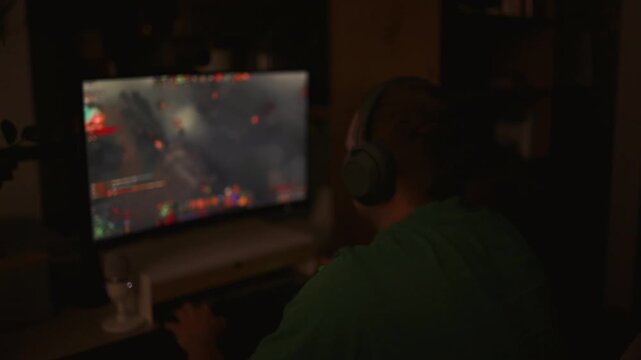 Caucasian teenager wearing headphones plays online video game on PC, spends leisure time at home. Professional young gamer enjoys gameplay in 3D third person shooter on computer. Gaming and Esports