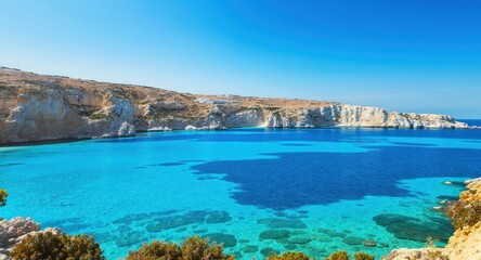 Naklejka premium Turquoise waters meet rocky cliffs under a bright blue sky, creating a scenic bay
