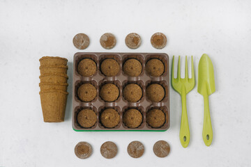 A small greenhouse with peat pellets for seeding, peat cups, and gardening tools on a gray background. Flat lay