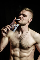 Against a black background, a sporty white man with a bare torso lights a cigarette from a burning photograph.