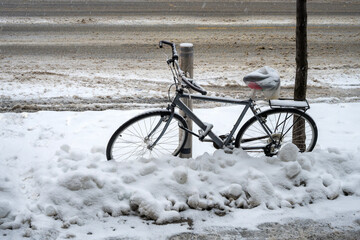 Bicycle buried under a thick layer of snow in Montreal. The bicycle is an urban model, with a wide saddle and raised handlebars. It is locked to a post with a lock