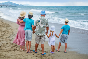 Happy large family standing on sandy beach, looking out ocean waves together, father with mother and children observing waves, family bonding during summer beach holiday getaway, school holidays