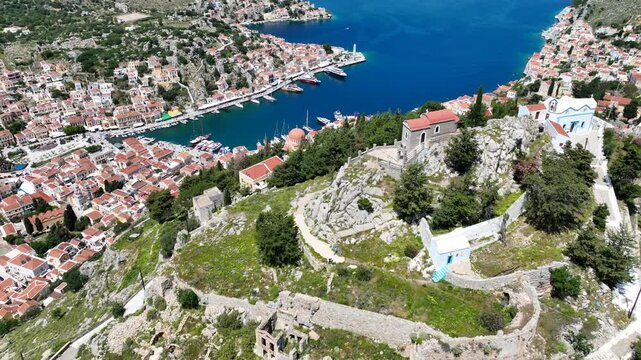 Aerial drone cinematic video of iconic castle of Symi island built uphill overlooking main town and Yalos, Dodecanese, Greece