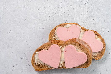 Two slices of bread with heart-shaped meat on top on a light surface seen from above during a simple meal preparation