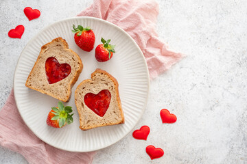 Toast with heart-shaped cutouts filled with jam and fresh strawberries on a plate with red heart decorations