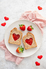 Toast with heart-shaped cutouts filled with jam and fresh strawberries on a plate with red heart decorations