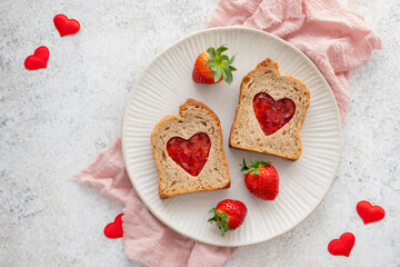 Toast with heart-shaped cutouts filled with jam and fresh strawberries on a plate with red heart decorations