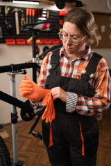 Female mechanic wearing gloves in bicycle workshop getting ready for professional bike repair service
