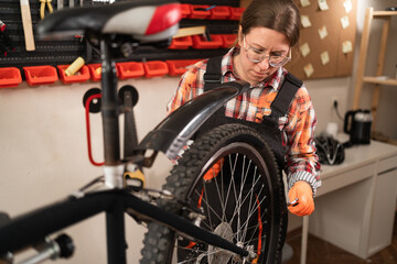 Female mechanic repairing bike rear wheel inside authentic workshop at night with professional tools