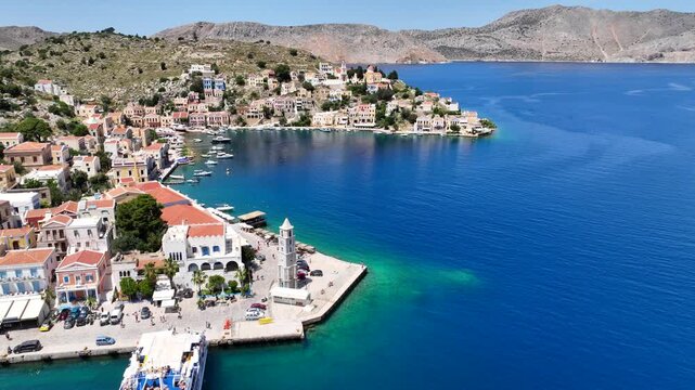 Aerial drone cinematic video of clock tower in main town and port of Yialos of Symi island with colorful neoclassical houses and traditional character, Symi island, Dodecanese, Greece