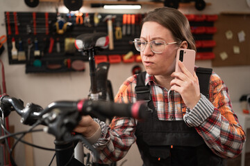 Female bicycle mechanic using a smartphone while repairing bicycle in garage or workshop.