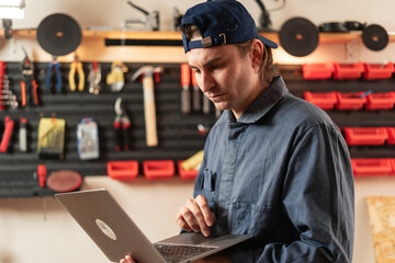 Portrait of confident small business owner craftsman using laptop at his workshop table