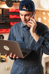 Small business owner carpenter talking on phone while using laptop in woodworking workshop. Male artisan discussing order with client and buying materials online