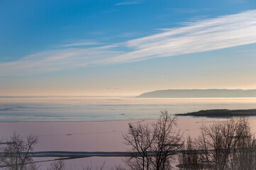 Winter landscape of a frozen river at sunset with blue sky and snow.