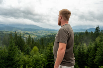 Thoughtful male traveler standing on a hill enjoying scenic summer landscape and cloudy sky