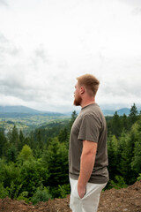 Side view of a young redhead man looking at the misty mountain valley and forest