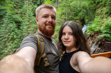 Young hikers couple taking selfie in summer forest near waterfall