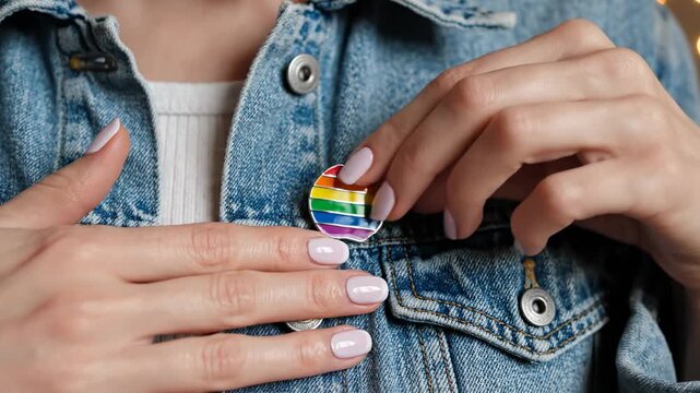 Close up view of hands fastening small rainbow pin onto denim jacket. Subtle gesture of lgbtq pride support and identity expression, symbolizing solidarity with community during pride month