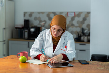 Muslim female researcher in hijab writing in notebook during work break at laboratory table