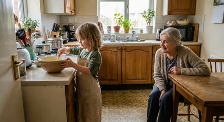 Young girl in apron stirs batter in large ceramic bowl while grandmother watches from table